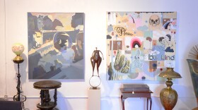 Paintings on canvas hang on a wall with brass lamps and art sculptures nearby.