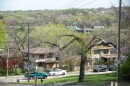 A pair of two-story houses sit in the foreground with cars parked in the street. In far background, a highway can be seen with traffic moving along it.