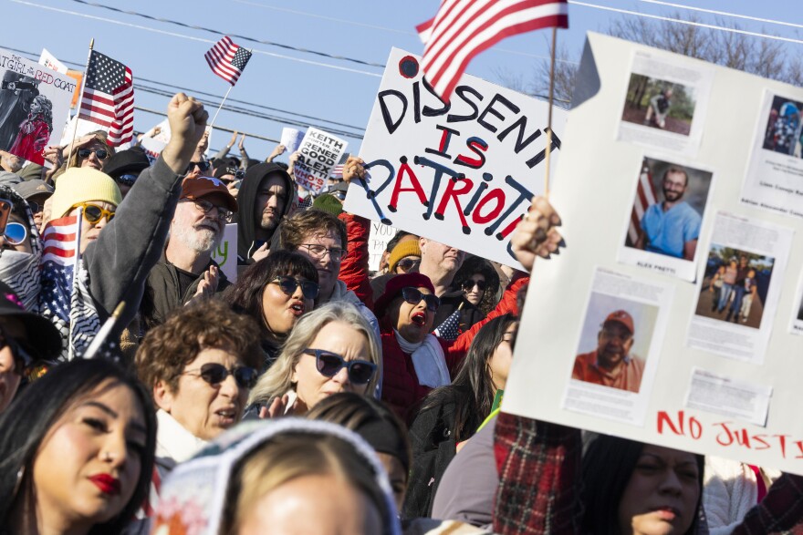 A large crowd holds up U.S. flags and signs at a protest.