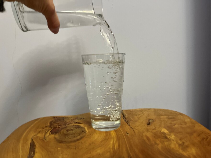 Water being poured into a clear pint glass on a wooden table.