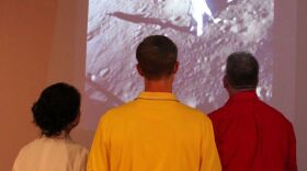 Three guests watch video of Apollo lunar landing during 2014 Moon Museum exhibition at Bob Rauschenberg Gallery