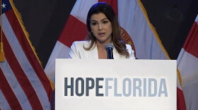 woman behind a podium that says Hope Florida speaks to an audience , american and florida flags are in the background 