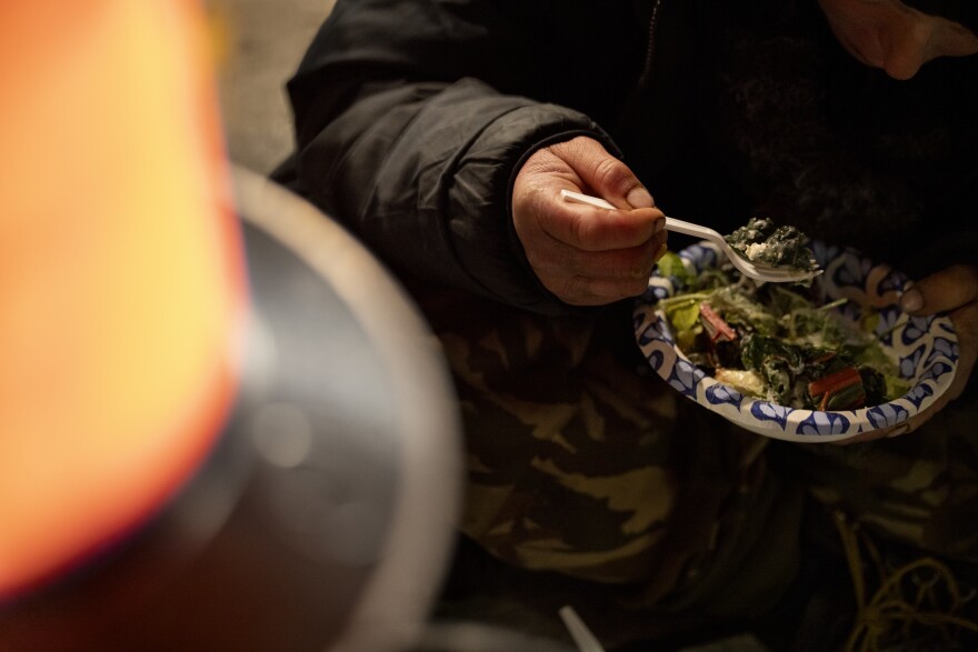 A person eats a plate of food near a heater.