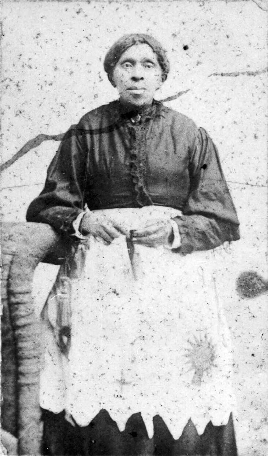 A black-and-white historical portrait of an African-American woman seated with a quilt square on her lap
