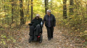 Man in wheelchair and woman walking use forest trail.