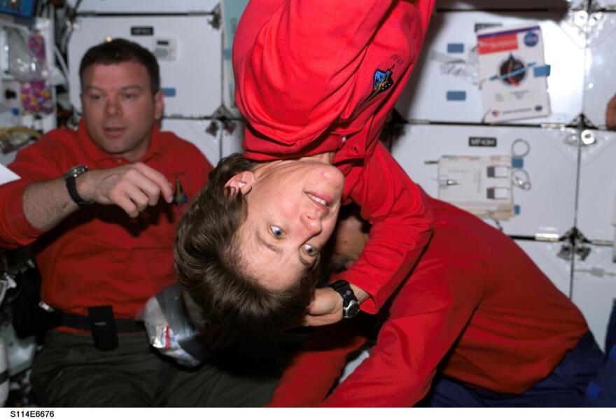 Astronaut Wendy B. Lawrence, STS-114 mission specialist, floats freely on the middeck of the Space Shuttle Discovery while the Shuttle was docked to the International Space Station. Astronauts James M. Kelly, pilot, and Charles J. Camarda, mission specialist, are visible in the background.