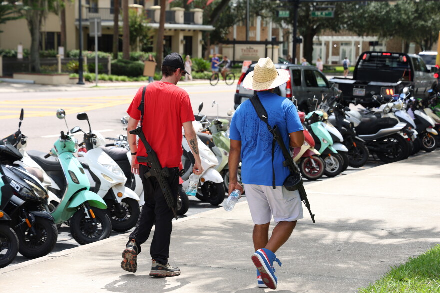 Two men who appear to be armed with rifles walk across from Tigert Hall, where protesters gathered, followed by a UFPD officer, in Gainesville Fla., Wednesday, Sept. 9, 2026. (Julianna Bendeck/WUFT News)