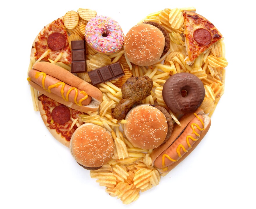 Various types of unhealthy food in the shape of a heart over a white background