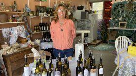 Woman smiling into the camera with bottles of olive oil on a table