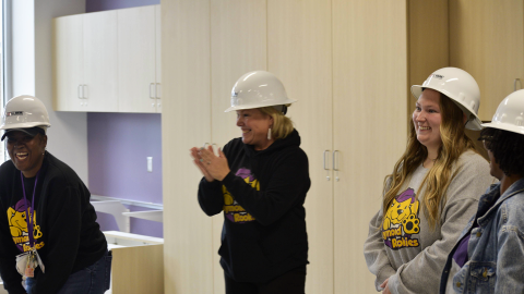 Women in hardhats clap and laugh in celebration.