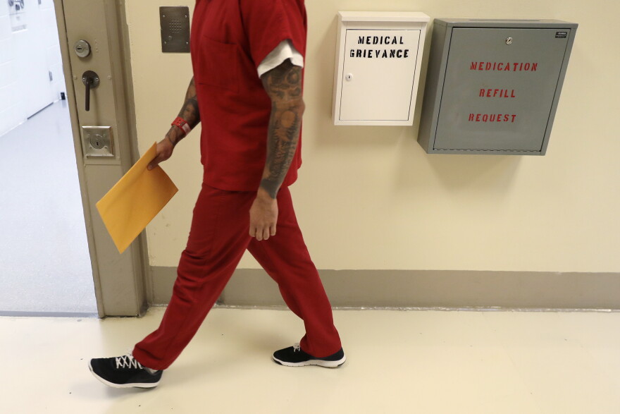 A person in an orange prison uniform walks down a hall. 