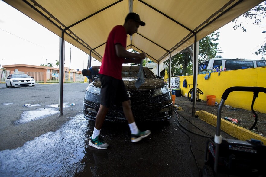 A worker at a pop-up car wash in Barrios-Bravos de Boston walks around a car he is cleaning. Several people lost their jobs after Hurricane Maria hit Puerto Rico. Unemployment remains high on the island and many here are doing everything they can to make ends meet. The U.S. Department of Labor reports the unemployment rate on the island was 9.1% in July down from 11% in November. (Jesse Costa/WBUR)