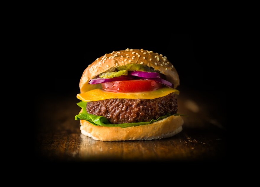 A cheeseburger sits on a wood counter against a black background.