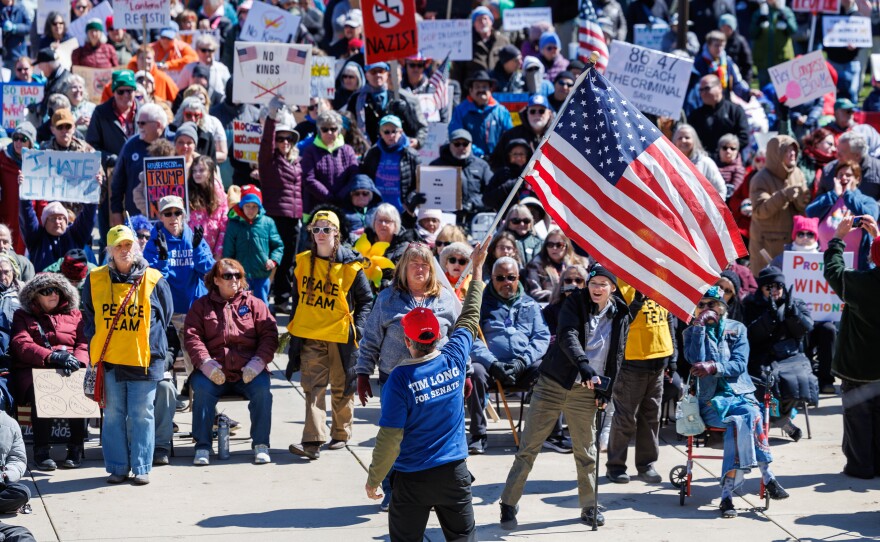 A supporter of President Donald Trump waves a flag in front of thousands of protesters during a No Kings rally at the Michigan Capitol in Lansing, Mich., on March 28, 2026.