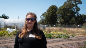 A woman stands in front of a small plot of land covered in drip irrigation tape with flowers in the foreground. 