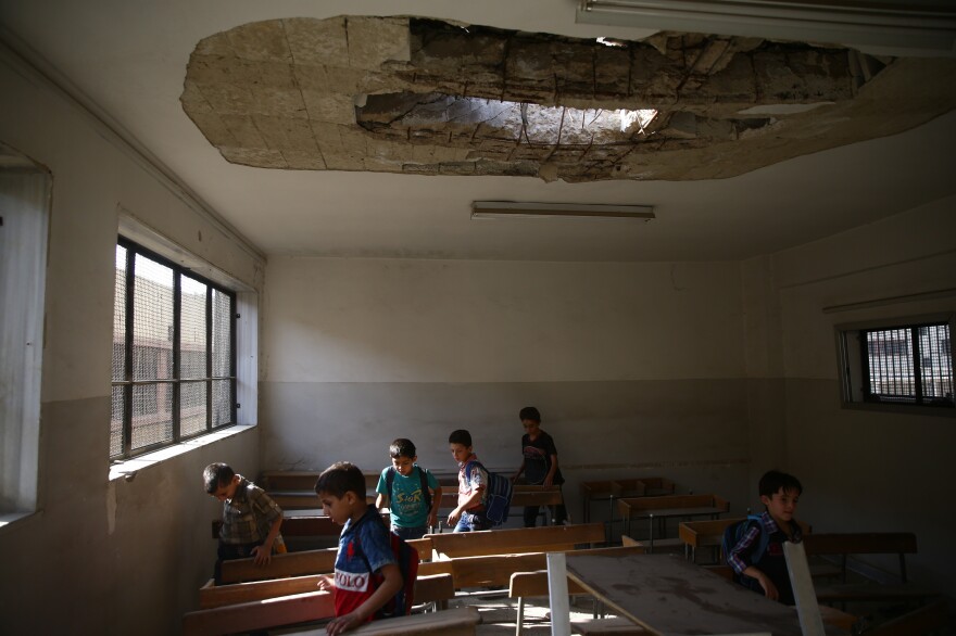 <strong>Sept. 16, 2017:</strong> <em>Douma</em> — Students enter a damaged classroom on the first day of school. In this area, the start of school was postponed due to large-scale aerial bombardment. A number of parents and communities have created battlefield and underground schools in the hopes of preventing a generation of Syrians from growing up without education.