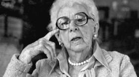 Black and white photo of an elderly woman with glasses staring into camera 