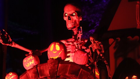 A fake skeleton with glowing eyes peering over a stone wall at the Jack O'Lantern Spectacular