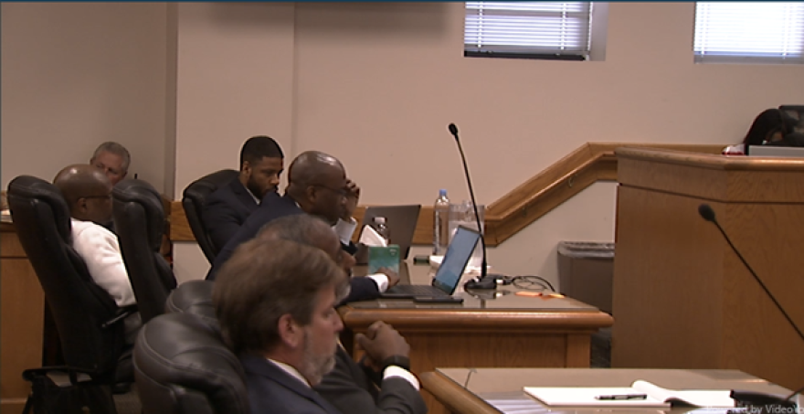 The defense and prosecution sit at their respective tables in a courtroom listening to testimony played back for the jurors.