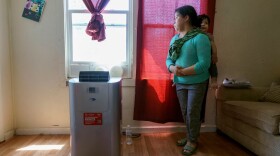 Woman with child on her back stands near a portable air conditioning unit
