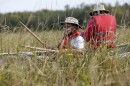 Two people sit in a canoe in a wild rice bed wearing life jackets and wide-brimmed hats