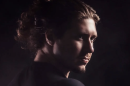 A man with a goatee and hair in a bun is staring off into the distance