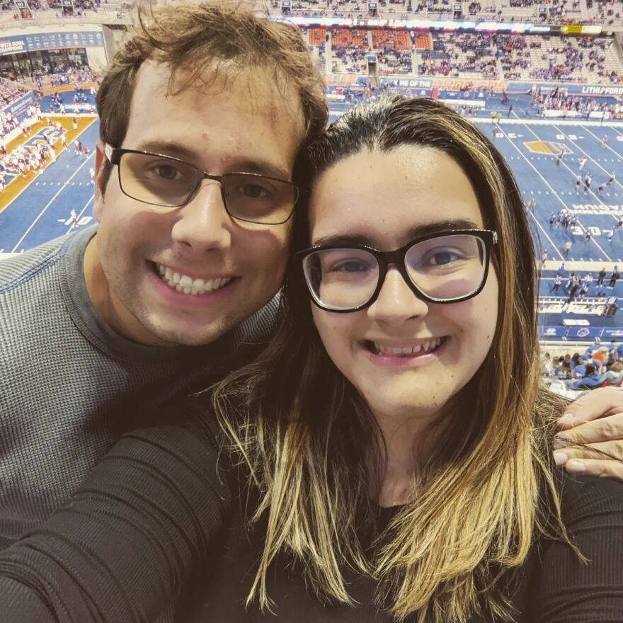 a man and a woman wearing glasses and smiling in front of a blue football field