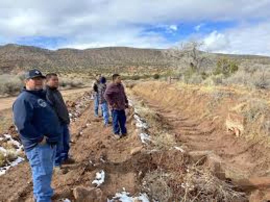 Daryl Lucero, Estevan Sando, and Arlan Sando, in the foreground, left to right, are members of the Jemez Pueblo in north-central New Mexico. They stand near a stretch of an earthen ditch on March 17th, 2023. For 40 years, the tribe has been working for a water rights settlement.