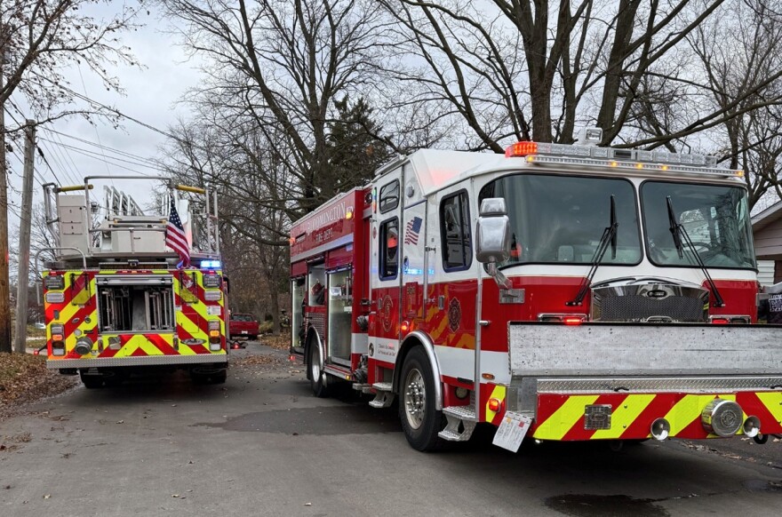 Two red fire trucks parked in opposite directions with flashing lights on a street outside a home