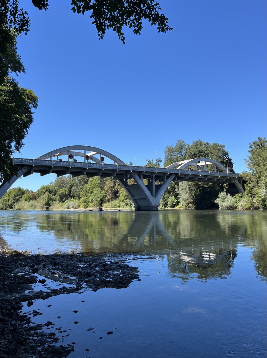 A large arched bridge is shown over a river, with blue sky and trees in the background. 