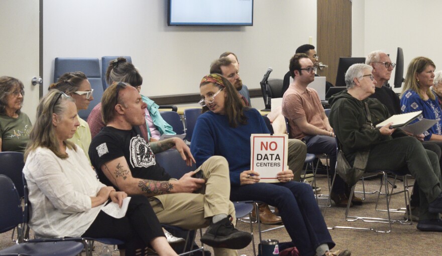 A woman holds a "No Data Centers" sign in the crowd at a city council meeting