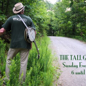 Image of man walking in tall green grass with banjo slung over his shoulder