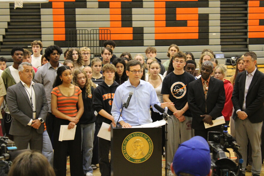 Gov. Bob Ferguson stands with students, teachers and administrators in front of a podium, inside the Lewis & Clark gymnasium. 