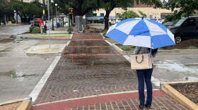 A woman waits in the rain to cross a downtown street on Oct. 2, 2026
