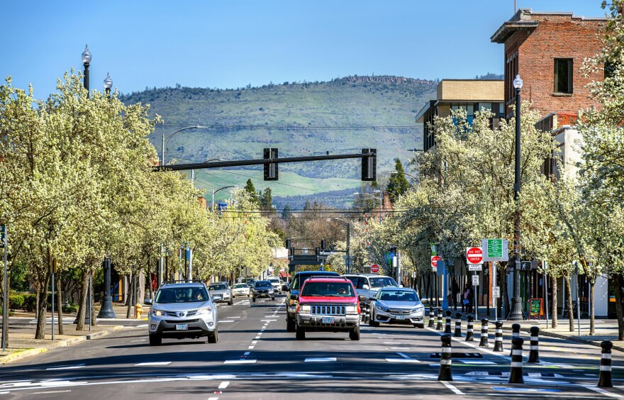 A straight-on view of a two-lane one-way street with parking on either side, and two bike lanes on the far right separated by bollards.