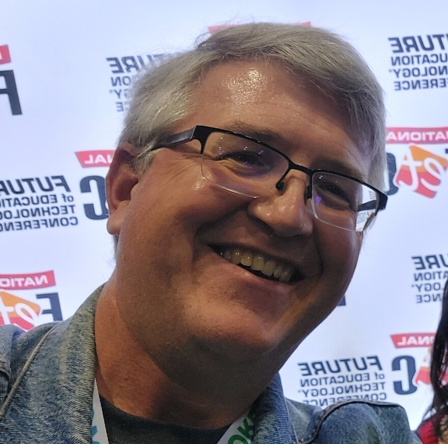 A headshot of gray-haired, bespectacled teacher Steve Conover, smiling at a teacher's conference