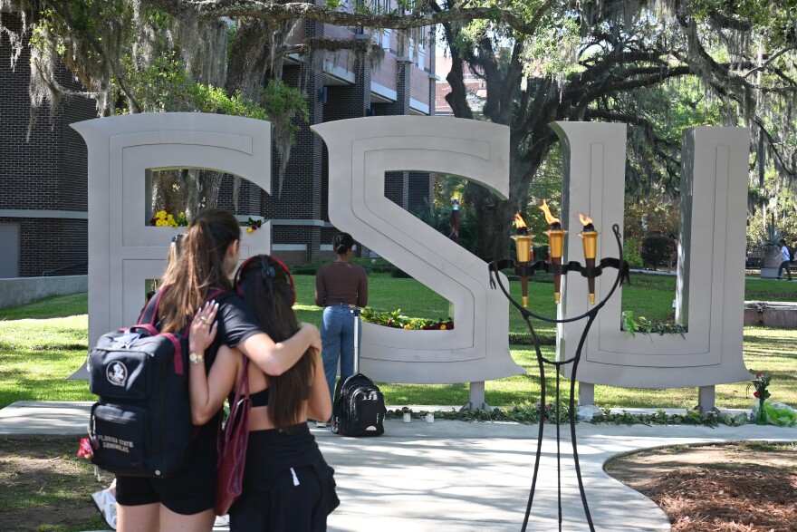 Two Florida State University students watch as others place flowers in front of the FSU letters outside of the university's student union on the anniversary of the campus shooting.