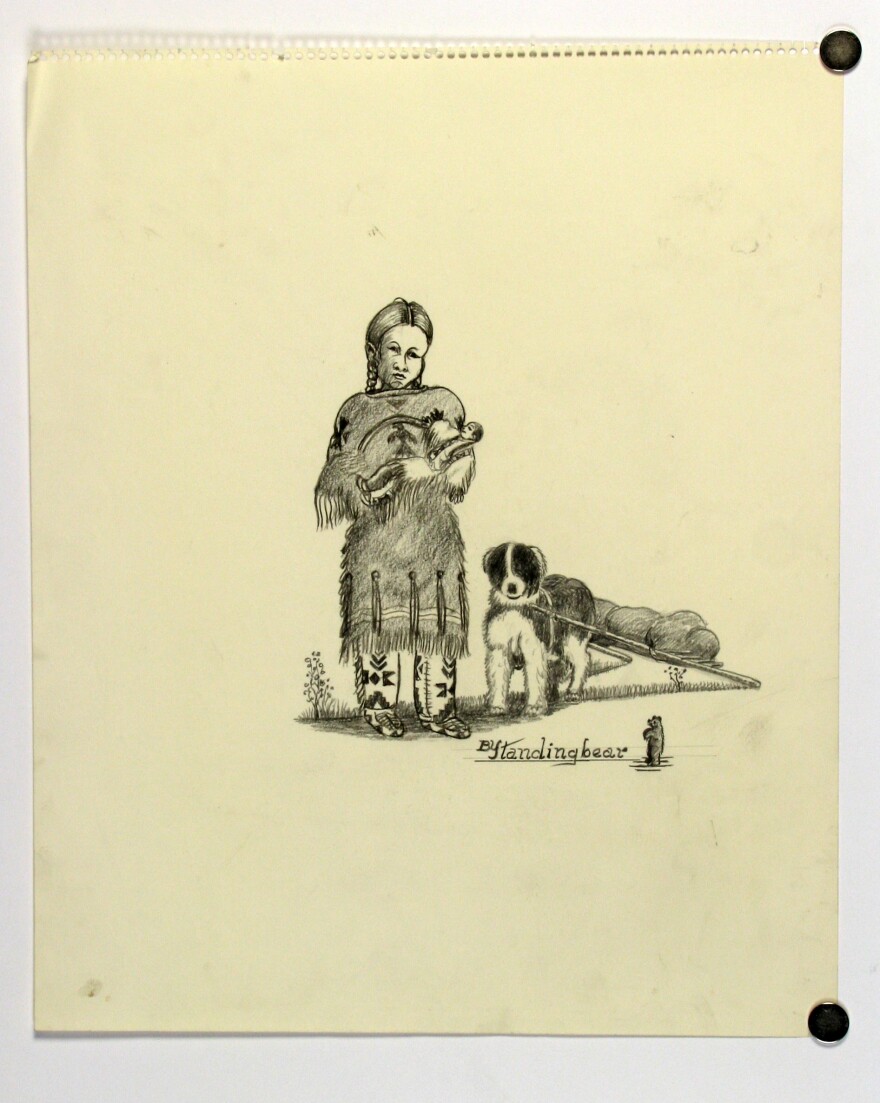 Pencil drawing on sketch pad paper depicting a young American Indian girl holding a doll. She wears a buckskin, fringed dress that falls to her knees. The bottom of the dress is decorated with a row of long strands of fringe held by buttons. Her knee high moccasins are decorated with geometric patterns. Her hair is parted in the middle and braided. Her doll is dressed in much the same way as the young girl. A dog with a travois sled carrying bundles is at her left side. The dog is black and white with fluffy fur. The drawing is inscribed with "BySandingbear", the "y" and "S" are merged as a single letter. A small standing bear is drawn next to the inscription.