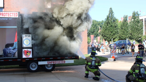 Two firefighters put out a fire in the "unprotected" section of the fire demonstration trailer with a hose.