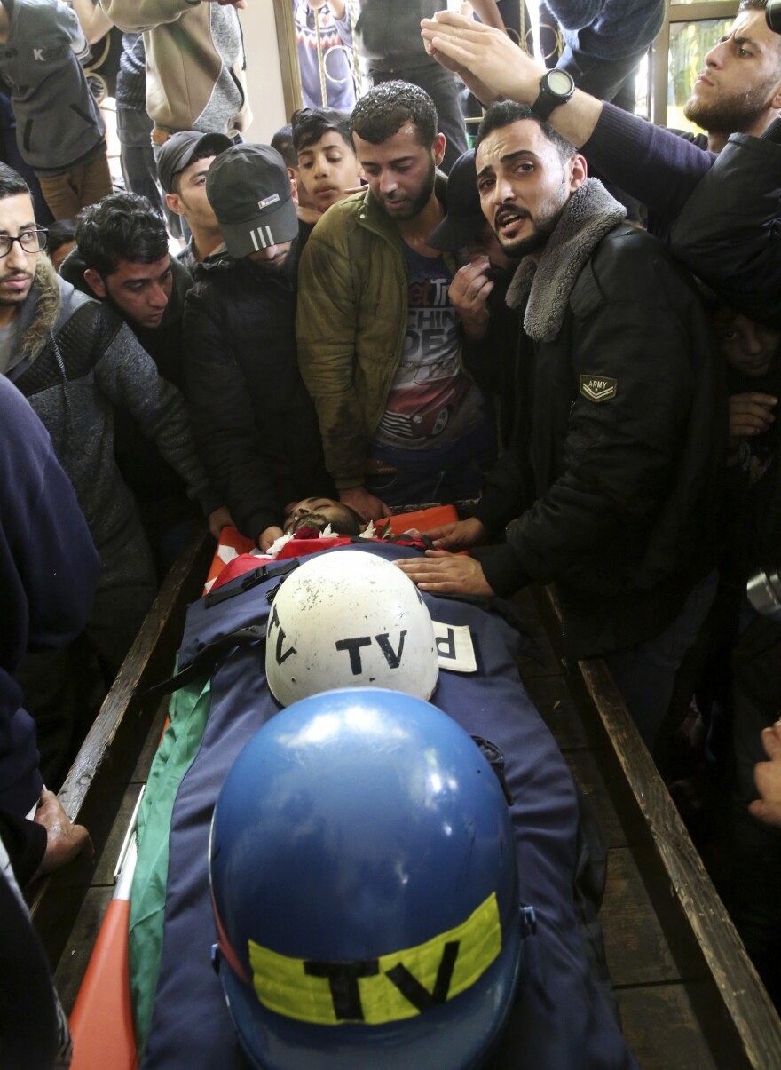 Mourners gather Thursday around the body of Palestinian journalist Ahmed Abu Hussein, who was killed by Israeli troops while covering a border protest. Resting with him are his helmets marking him a member of the television media.