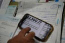 A phone zoomed in on a photo of a high utility bill. The bill is for $2,300.17. Behind the phone are other bills and bookkeeping paperwork. 