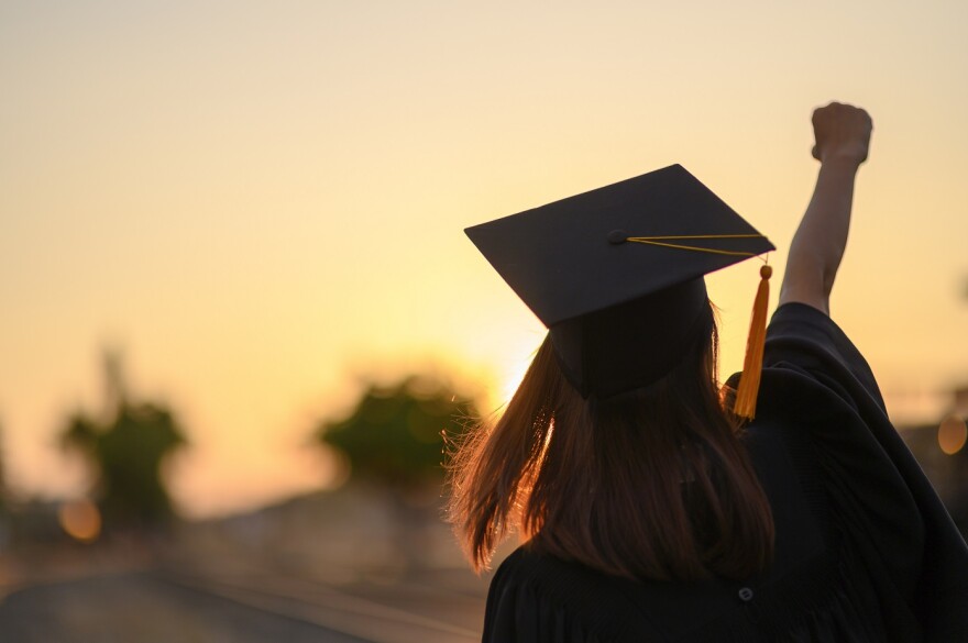 Graduate in cap and gown pumps fist and looks into the sunset.