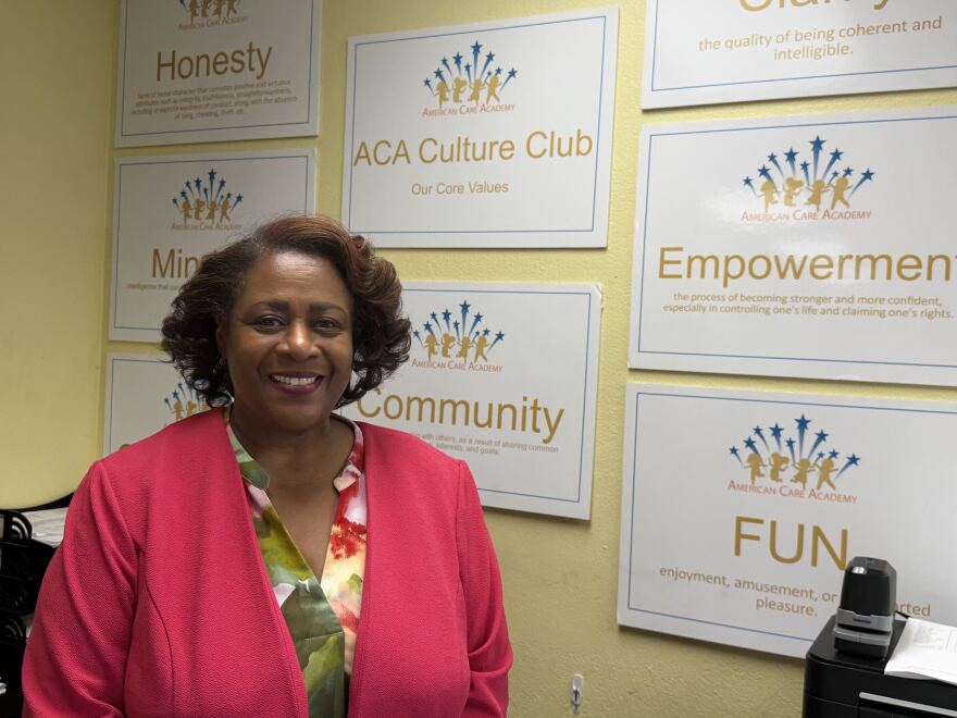 A Black woman in a pink blazer stands in front of a wall with signs