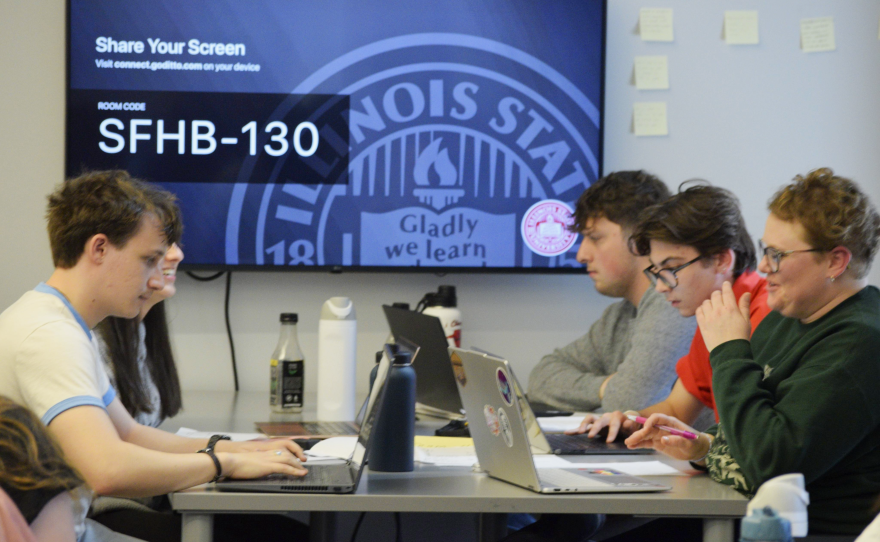 Students use laptops while they sit together at a tall table.