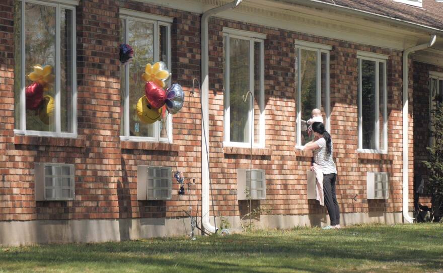 A woman holds up a baby to a window outside the Kimberly Hall South in Windsor to visits with a resident on May 5. (Dave Wurtzel/Connecticut Public)