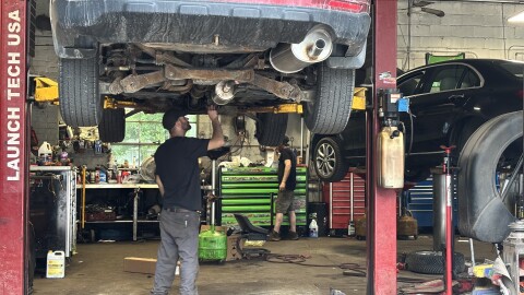 A mechanic stands under a vehicle on a lift 