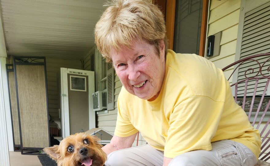 A photo of an older woman with a small dog on her porch. 