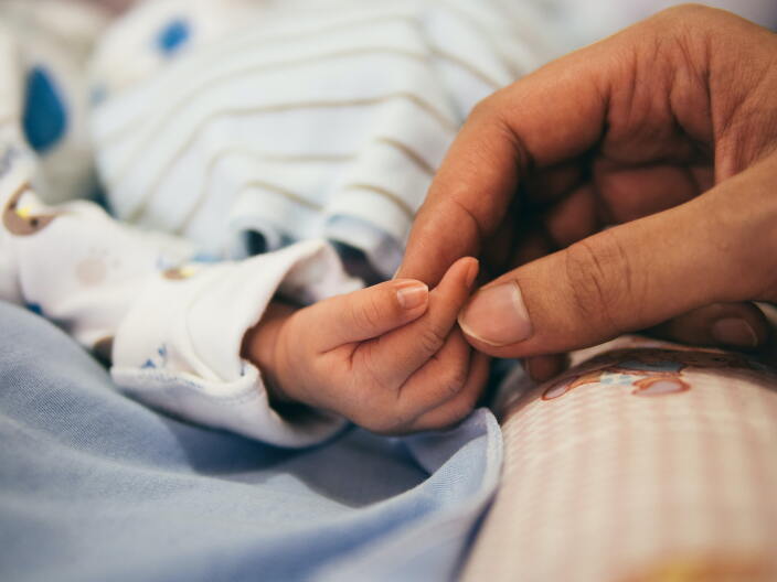 A mom's hand touches a newborn's fingers