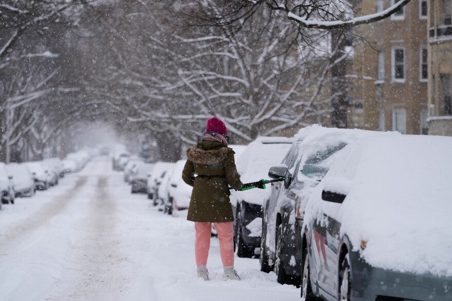 A person cleans the snow from a car during a snowy day in Chicago, Sunday, Jan. 25, 2026.