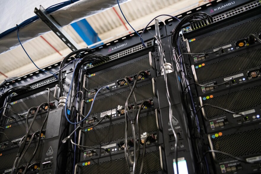 Black servers with cables coming out of them and extending up towards the ceiling.